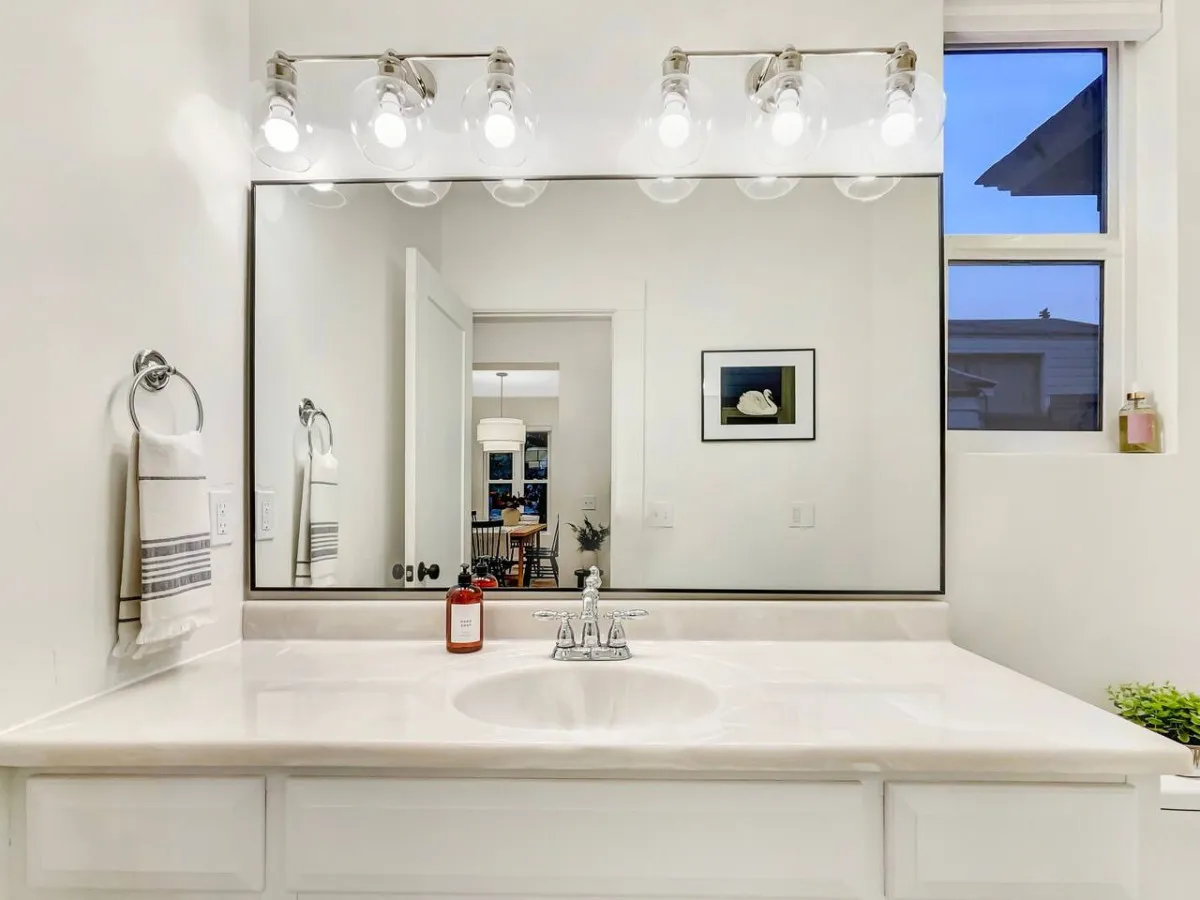 A stylish bathroom featuring a mirror with lighting, a sink with a modern faucet, and decorative items on the counter. The environment is serene and clean, perfect for relaxation and self-care routines.