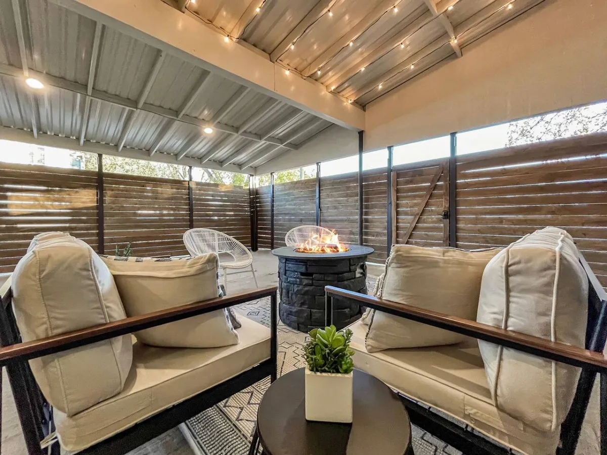 A cozy outdoor seating area centered around a glowing fire pit. Comfortable chairs and decorative plants enhance the ambiance, creating a welcoming environment for socializing and storytelling. The warm light of the fire makes the space feel inviting and perfect for evening gatherings.