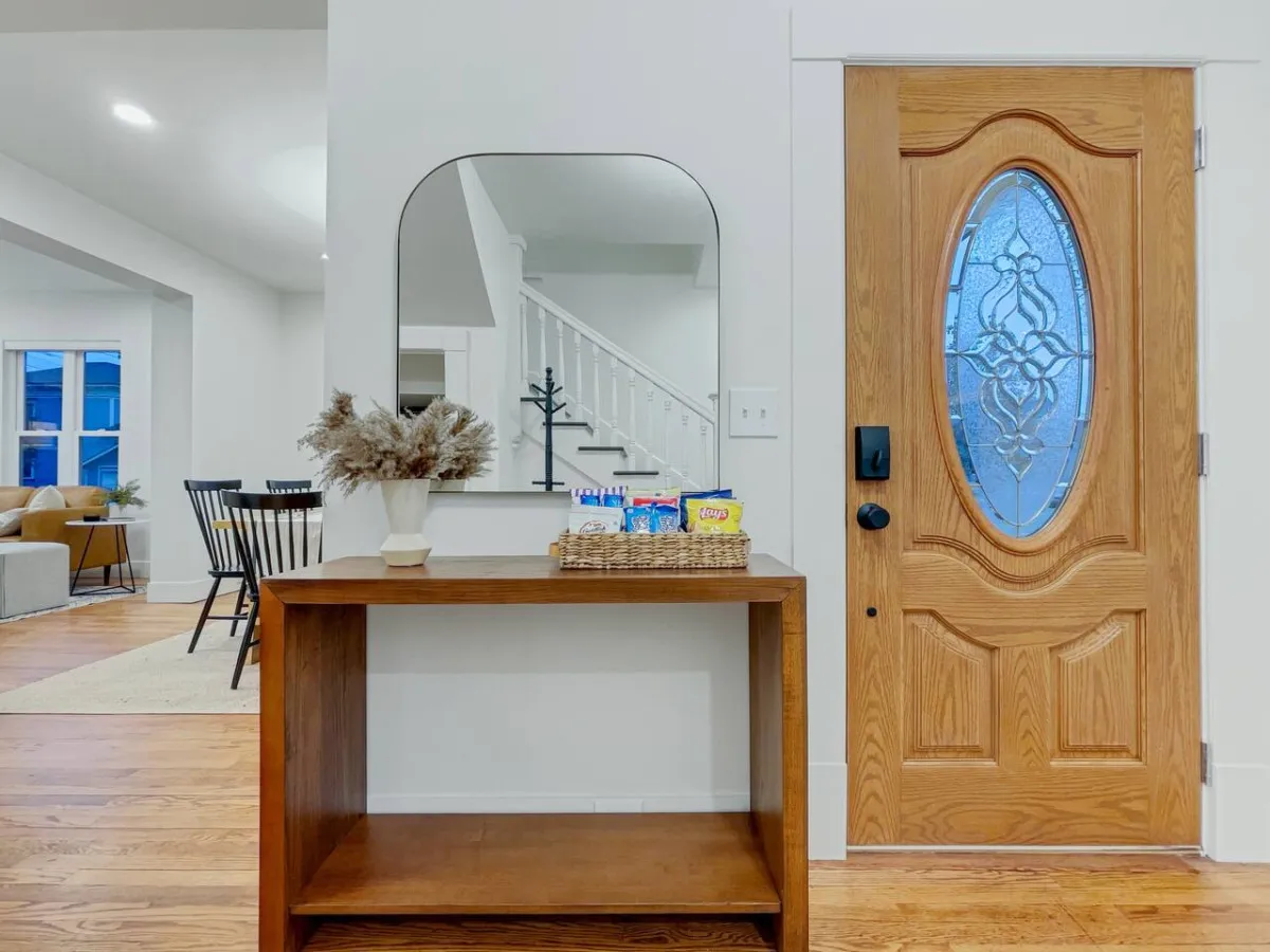 The home's entryway with a wooden entry table, decorative mirror, front door, and a tasteful plant arrangement. The space feels immediately inviting and offers a warm welcome to arriving guests.