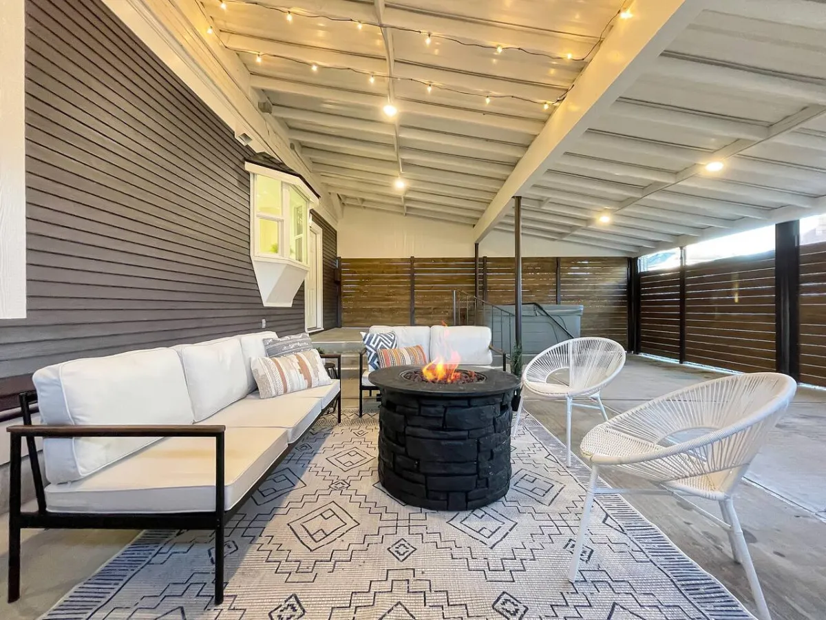 A stylish outdoor area featuring a fire pit, sofa, acrylic chairs, and a patterned outdoor rug. The setting sun casts a golden glow, suggesting evening relaxation and memorable gatherings.